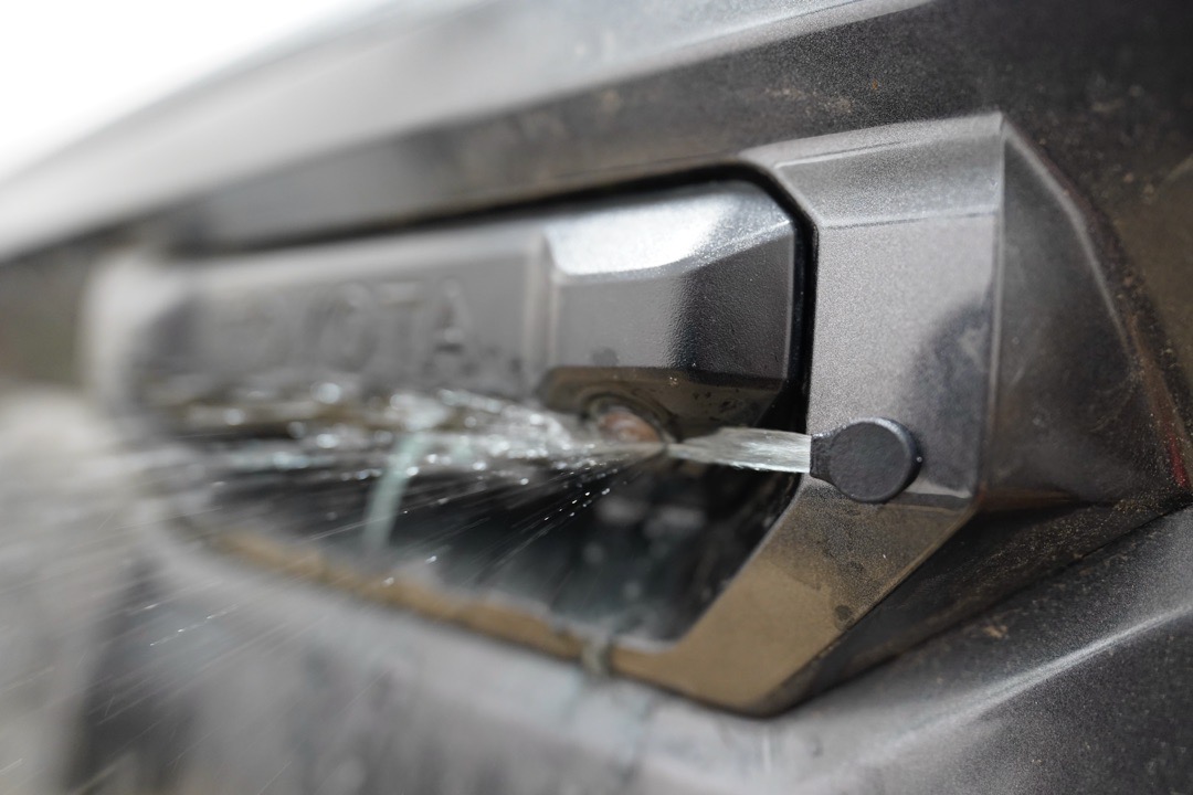 Close-up spray clearing a muddy Toyota Tacoma camera